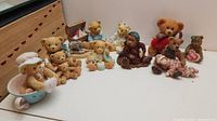 Collection of 12 teddy bear figurines on a flat surface including bears in varied outfits and poses