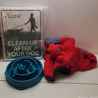 Photo showing a blue slow feeder dog bowl, large red dog sweater, and one 'Please Clean Up After Your Dog' sign wrapped in bubble wrap.