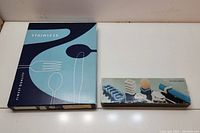 Photo of the boxed flatware set and box of ceramic spoon rests on white surface