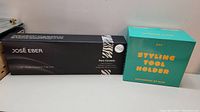 The flat iron in its black box with branding showing José Eber and pure ceramic plate information alongside the turquoise box for the styling tool holder.