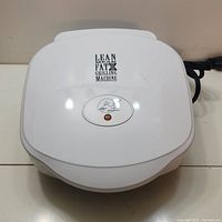 Closed top view of George Foreman grill showing white plastic casing with branding and power cord on the side