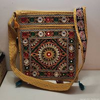 Front view of the yellow fabric shoulder handbag showing multicolor embroidery, circular mirrors, and tassels