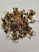 Top-down photo showing multiple gold-tone jacket pins with green jade stones and safety chains piled together.