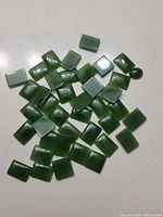 Photo of approximately 40 polished dark green jade stones concentrated mostly in rectangular shapes with a single oval-shaped piece