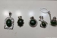Five jade jewelry pieces arranged in a row on white surface: four pendants and one jacket pin.