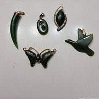 Lot of five green jade pendants arranged on flat surface with coin for scale, showing various shapes and metal accents.