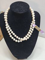 Front view of double-strand pearl necklace on black jewelry display stand showing Kimono brand lavender ribbon tag.