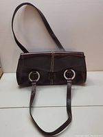 Brown leather purse with double straps and silver-tone ring details lying on white surface.