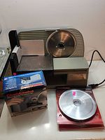 Photo showing the entire setup including the Chef's Choice electric meat slicer, diamond wheel sharpener in original box, and two extra replacement blades in packaging.