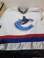 White Vancouver Canucks jersey laid flat showing the full front with the team orca logo, neckline, and hem stripes.