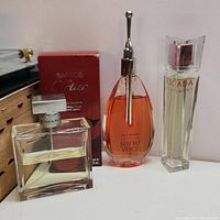 Four perfume bottles including Escada Sentiment, Sotto Voce, Ralph Lauren Romance, and Santos De Cartier with box arranged side by side