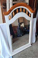 Front view of standing mirror showing white frame with natural wood curved top and spindle accents.