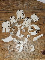 Top view of the white pendants and earrings spread on wood surface with a penny for scale, showing elephant, shell, horn shapes, and spherical beads.