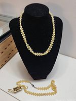Two yellow jade and pearl bead necklaces displayed on a black jewelry bust and lying flat.