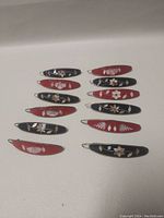 Top side view showing all 12 oval pins in alternating black and red backgrounds with silver floral and leaf designs.