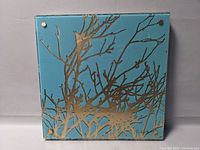 Abstract art piece showing brown tree branch pattern on blue background, mounted with metal fasteners at corners.