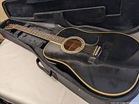 Black American Legacy acoustic electric guitar inside a soft or hard case, shows the body and fretboard with cream binding and steel strings.