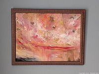 Frontal view of the framed abstract painting featuring pink and red hues resembling a dynamic sky scene.