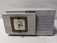 Front view showing the GE Musalarm clock radio with psychedelic patterned bakelite case, clock face with bronze frame, radio tuner dial, and control knobs.