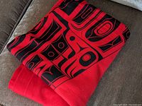 Photo of folded red Haida blanket showing red fabric and black design detail.