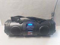 Front view of JVC Kaboom portable boombox with visible speakers, control panel, carrying strap, and power cord.
