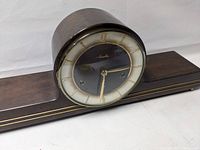 Front view of the mid century mantel clock showing its round face, gold numerals, and wooden base with gold trim.