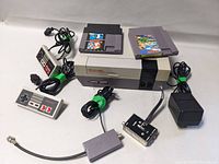 Photo showing the NES console with two game cartridges, two wired controllers, RF switch, and power adapter.