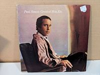 Front cover of Paul Simon 'Greatest Hits, Etc.' vinyl LP album featuring a seated portrait of Paul Simon in color tone.