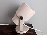 Side view of the white metal spot light lamp showing cylindrical housing and round base with adjustment knob on the side.