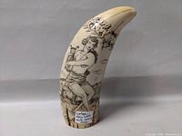 Full view of the ivory-toned resin whale tooth shaped carving showing a man playing a harp and nature scene.