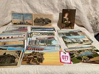 Wide view of over 100 vintage postcards spread out showing a variety of subjects including a tall building, various landscapes, and other historical scenes.