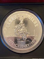 Close-up of reverse side of 1975 Canadian silver dollar showing cowboy on bucking bronco and Calgary cityscape