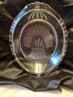 Top-down view of the clear pressed glass bread dish showing detailed etched wheat sheaf design in the center and text around rim.