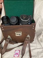 Brown leather camera bag open showing contents including lenses and accessories