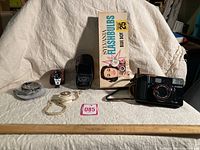 6 items displayed including Canon camera, Sylvania flash cubes, light meter, watch, and accessories on fabric background