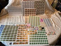 Wide view showing multiple sheets of Canadian mint stamps laid out on a cloth surface, including multiple denominations and designs