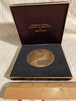 Photo of the bronze medal in original presentation case showing 'International Film & TV Festival New York' on the interior lid with the medal in the velvet insert below along with a measuring ruler showing scale.