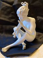 Full view of the white bisque porcelain figurine of a seated nude child playing pipes