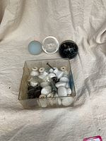 Overall view of two signed glass paperweight spheres and small opaque glass sphere, with a plastic container holding multiple white and black ceramic door knobs, some attached to screws.