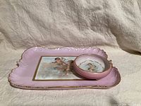 Pink rectangular porcelain tray with cherub and gilt edges on a fabric background