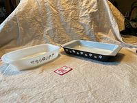 Photo showing two vintage Pyrex casserole dishes side by side on cloth background; white dish with brown floral design and black dish with white floral design.