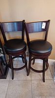 Pair of dark brown wood swivel bar stools with black round padded seats in front of wall