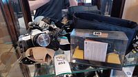 Canon AE-1 camera with strap and Kodak camera in case with manual on glass shelf