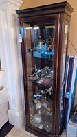 Full height view of wooden display cabinet with glass door and shelves showing silverware and collectables inside (not included)