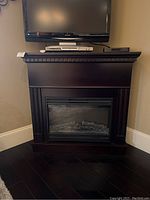 Full view of a dark brown wood finish electric fireplace with faux logs inside, positioned against a wall and under a mounted flat screen TV.