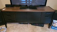 Front view of the entertainment stand with a TV on top and black drawers and cabinets below.