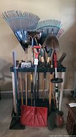 Photo showing assortment of garden tools including rakes, shovels, and hoe held in a black plastic tool caddy stand