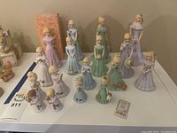 Front view of all 16 Growing Up Girls figurines arranged by increasing age, showing details of dresses, faces, and age numbers.