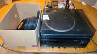 Kenwood turntable on top of Kenwood receiver with a large cardboard box filled with vinyl record albums beside them.