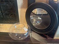 Photo showing the round mirror with a wide black wooden frame and the large clear glass bowl side by side on a wooden surface.